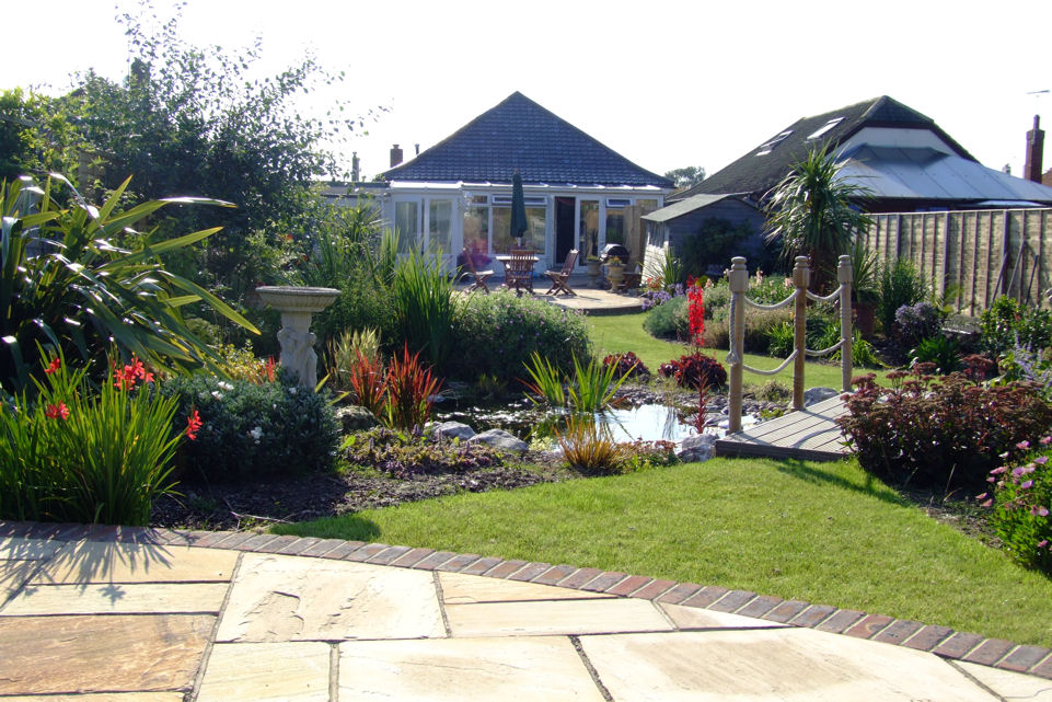 garden design Bridge over pond to two indian sandstone seating areas mediteranian and traditional English planting styles constantly evolving throughtout the year
